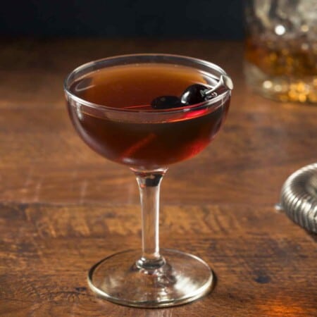 Manhattan cocktail with Maraschino cherries on wooden table